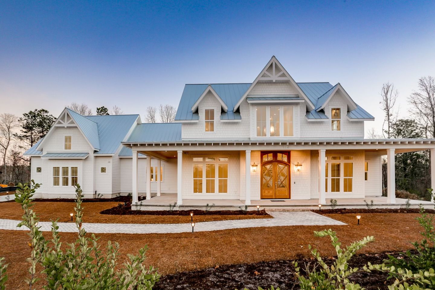 Completed white farmhouse with metal roof at dusk